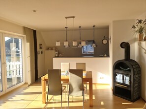 A dining area with a wooden table and chairs, a kitchen with a built-in oven, and a large window.