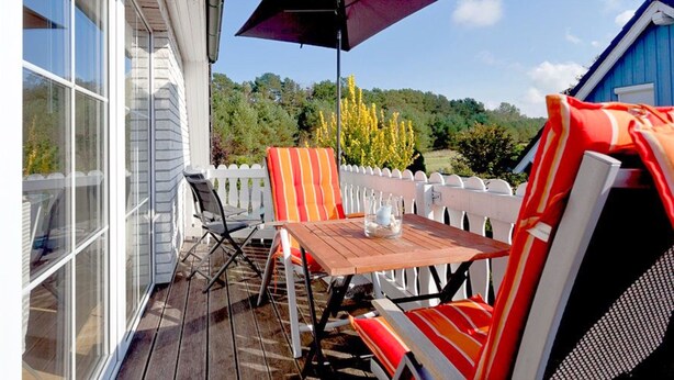 An outdoor patio with a table and chairs, a large umbrella, and a view of a forested area.