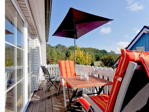 Une terrasse extérieure avec une table et des chaises, un grand parasol et une vue sur une zone boisée.