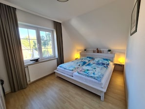 A bedroom with a bed, a window with curtains, a radiator, and a nightstand with a lamp.