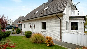 Ein eingeschossiges Haus mit geneigtem Dach, einer Ziegel-Fassade und einem weißen Zaun.