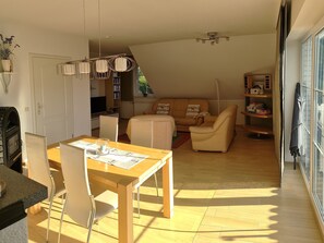 A living room with a sofa, a dining table with chairs, a TV, and a bookshelf.