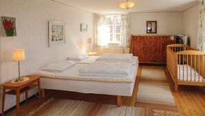 A bedroom with a large bed, a wooden crib, a nightstand, a lamp, and a window with curtains. - Stunning home in Hovmantorp with WiFi (Hovmantorp)
