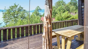 Une terrasse en bois avec une balançoire, une table et une vue sur la mer et la verdure.