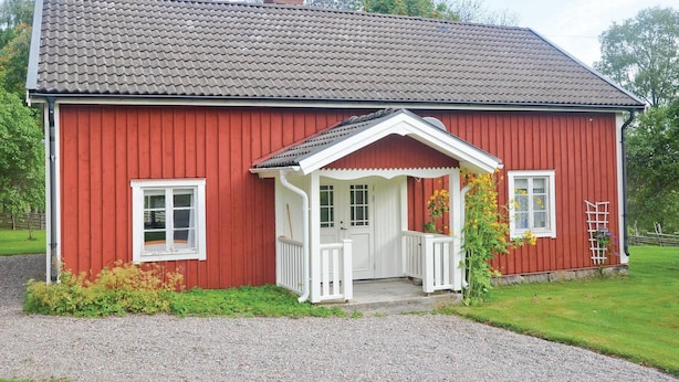 Una casa de madera roja con un porche blanco y un camino de grava.
