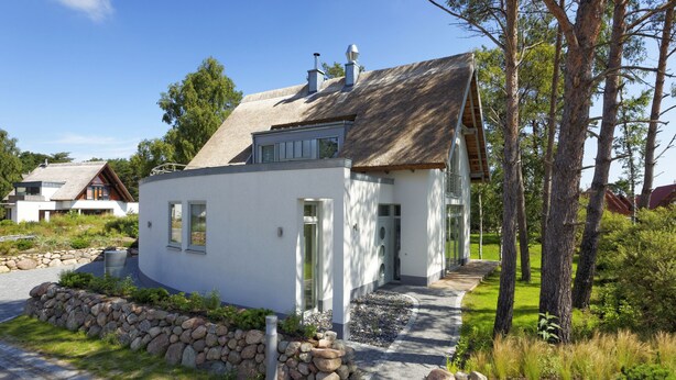 Una casa moderna de color blanc amb fonaments de pedra, un teulat de palla i un camí de pedra que porta a l'entrada.