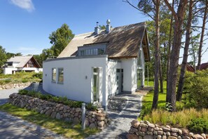 A modern white house with a stone foundation, a thatched roof, and a stone pathway leading to the entrance.