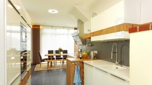 Una cuina moderna amb armaris blancs, una illa de fusta i una zona de menjador amb taula i cadires.