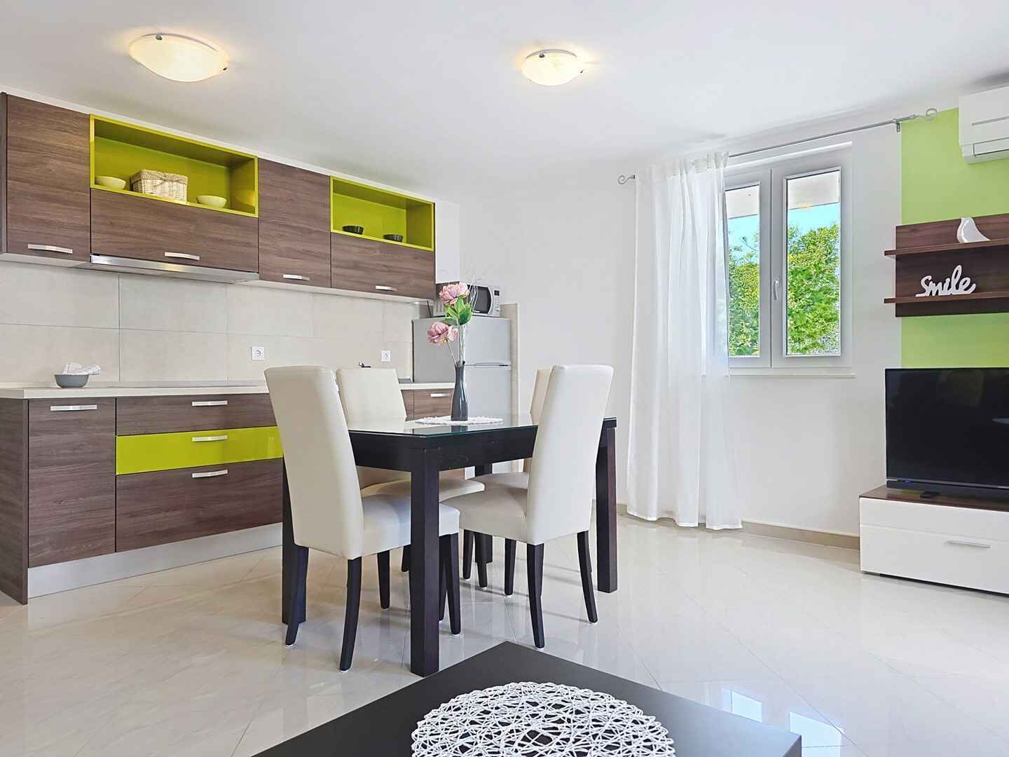 Eine moderne Küche mit Holzschränken, einem Esstisch mit Stühlen, einem Fernseher und einem Fenster mit Vorhängen.