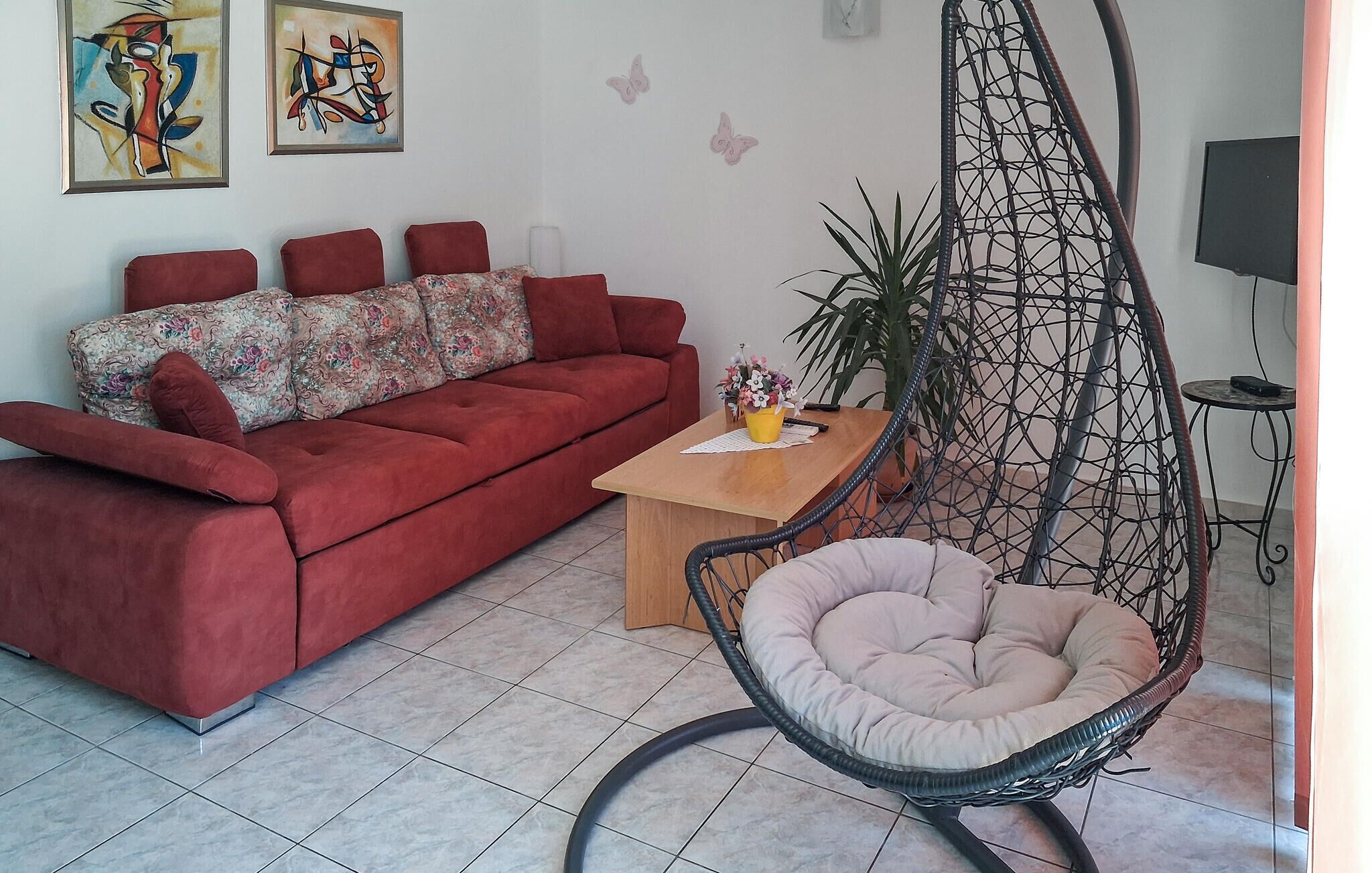 A living room with a red sofa, a wooden coffee table, a hanging chair, and two abstract paintings on the wall.