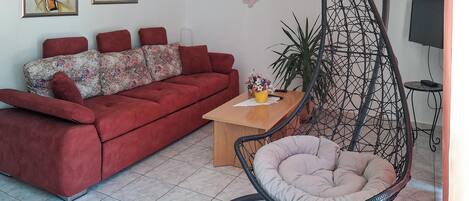 A living room with a red sofa, a wooden coffee table, a hanging chair, and two abstract paintings on the wall.