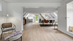 Ein geräumiger Loft mit hohen Decken, freiliegenden Holzbalken und einem zentralen Essbereich mit Treppe.
