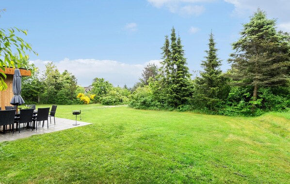 A grassy backyard with a patio table and chairs, surrounded by trees and a wooden fence.