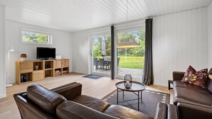 Ein geräumiges Wohnzimmer mit einer Ledersofa, einem Couchtisch und einem Fernseher auf einer Holzkommode. Eine Glasschiebetür führt zu einer Außenpatio mit Tisch und Stühlen.
