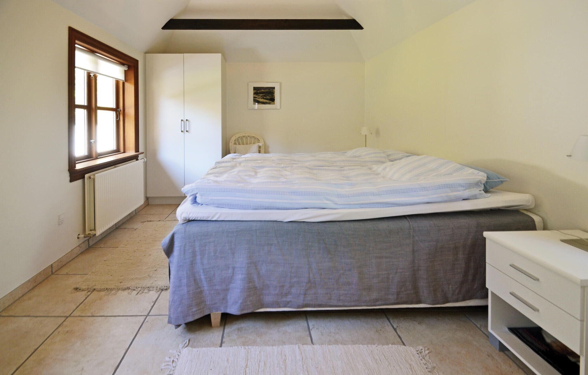 A bedroom with a bed, a nightstand, a wardrobe, and a window.