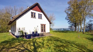 Ein weißes Haus mit rotem Dach, einer kleinen Veranda mit Stühlen und Blick auf einen See.