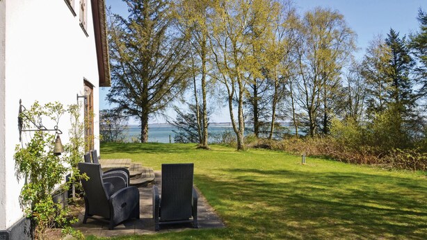 Eine Terrasse mit Gartenmöbeln, Blick auf das Meer und Bäume.