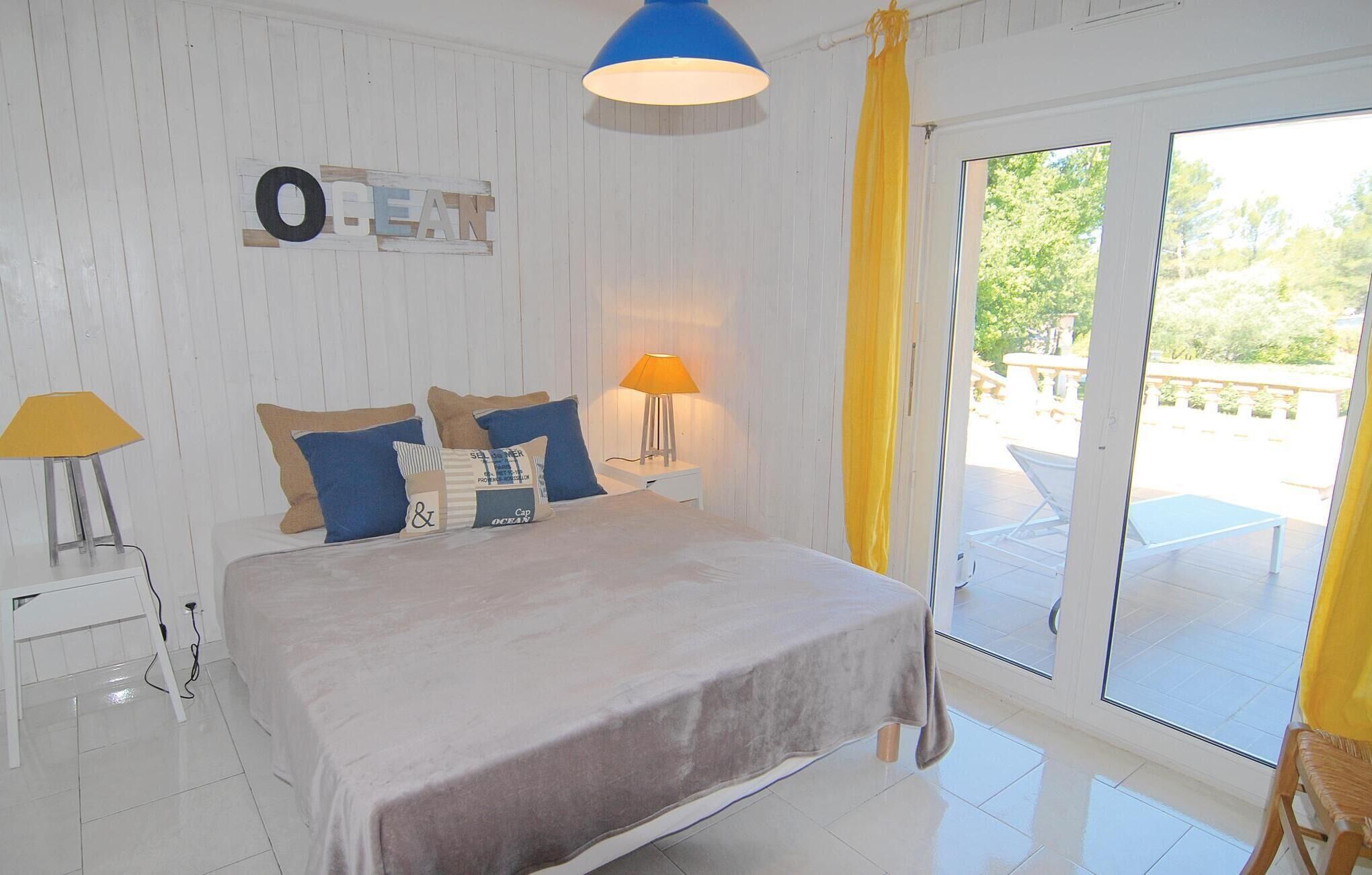 A bedroom with a bed, two bedside tables, a lamp, and a view of the outdoors through a sliding glass door.