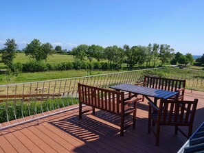 A wooden deck with a table and chairs, overlooking a green landscape with trees and a fence. - Ferienwohnungen Ostseeblick (Kronsgaard)