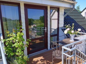 A covered outdoor area with a sliding glass door, a metal table with chairs, and a potted plant. - Ferienwohnungen Ostseeblick (Kronsgaard)