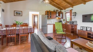 Un salón acogedor con un sofá, una mesa de comedor y sillas. Se ve una cocina con armarios de madera y un refrigerador al fondo.