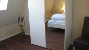 A bedroom with a bed, a bedside table, a nightstand, a window, and a plant. - 4-room 205 Norderney 3Balk Spülm. 2Bäder (BC 5) - BUE - Appartementhaus Westwind (Büsum)