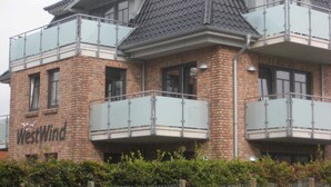 A multi-story building with a brick facade, large windows, and balconies with glass railings. - 4-room 205 Norderney 3Balk Spülm. 2Bäder (BC 5) - BUE - Appartementhaus Westwind (Büsum)
