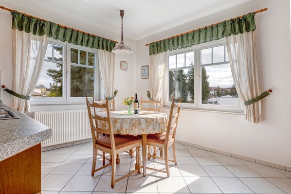 A dining area with a round table, wooden chairs, and a window with curtains.