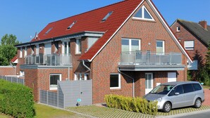 Et toetages murhus med rødt tag, en balkon på øverste etage og en bil parkeret i indkørslen.