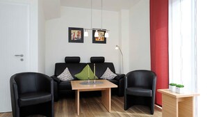 En moderne stue med en sofa, to sorte lænestole, et træ sofabord og et lille sidebord med en plante.