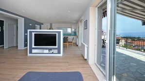 Un salon moderne doté d’un grand téléviseur à écran plat, d’un parquet et d’un balcon avec un sol en pierre offrant une vue sur la mer.