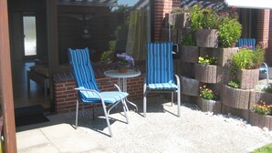 An outdoor patio with two striped chairs, a small round table, and a brick wall with planters.
