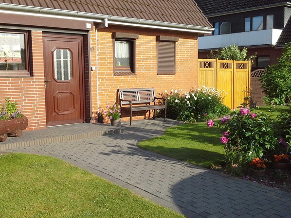 A residential house with a brick facade, a wooden door, a bench, and a garden with flowers and a wooden fence. - 2 Terr re (BC.n3) - BUE - Ferienhaus Helmcke (Büsum)