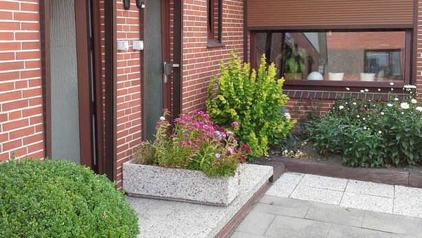 A brick building with two doors, a small window, and a garden with various plants and flowers.