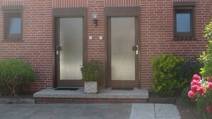 A two-story brick building with two doors, a small window, and a potted plant in front.