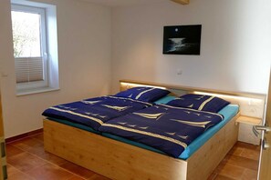 A bedroom with a wooden bed, a window with blinds, and a wall-mounted picture. - Apartment "Summer Room" - Rügen-Fewo 279/2 (Putbus)