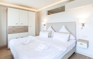 A modern hotel room with a large bed, a wardrobe, a bedside table, and a wall-mounted light fixture.