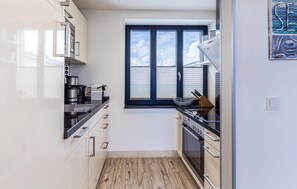 A modern kitchen with white cabinets, a black countertop, a window with blinds, and a built-in oven.