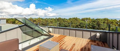 A rooftop terrace with a glass balustrade, wooden flooring, and outdoor furniture.