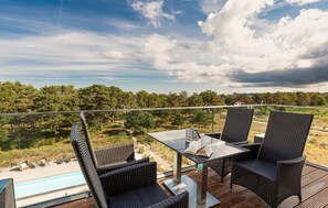 Una terraza con sillas de mimbre y una mesa, con vista a una piscina y un paisaje boscoso.