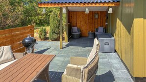 Een terras met rieten meubilair, een barbecue en een overdekte zithoek.