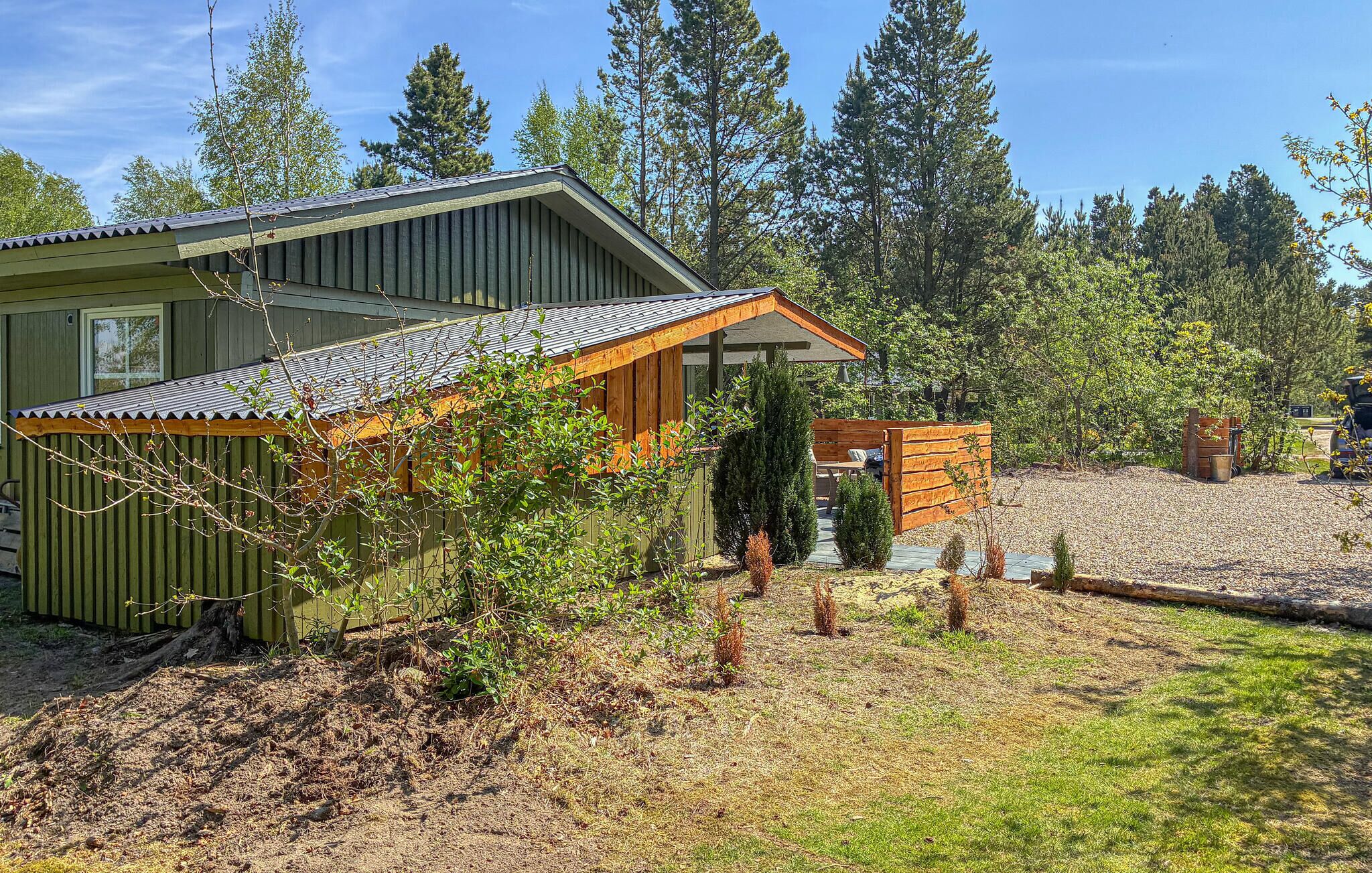 A green building with a sloped roof and a wooden structure in front.