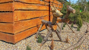 Een houten constructie met een gevlinderd ontwerp, mogelijk een schuur of tuinhuis, omringd door grind en kleine planten.
