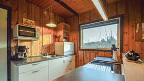 Een compacte keuken met houten wanden, een ingebouwde magnetron, een koffiezetapparaat en een raam met uitzicht op bomen.