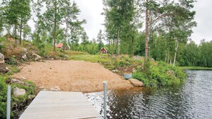 A wooden dock leading to a sandy beach area with a small house in the background. - Stunning home in Holmsjö with kitchen (Holmsjö)