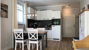 A modern kitchen with white cabinets, a dining table with four chairs, and a wicker chair in the corner. - (178) 3-room apartment Ostseeallee - apartment house Dünenschloss (Kühlungsborn)