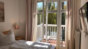 A bedroom with a bed, a bedside lamp, a TV, and a balcony with curtains. - (178) 3-room apartment Ostseeallee - apartment house Dünenschloss (Kühlungsborn)