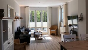 A modern living room with a sofa, a dining table, wicker chairs, and a TV. - (178) 3-room apartment Ostseeallee - apartment house Dünenschloss (Kühlungsborn)