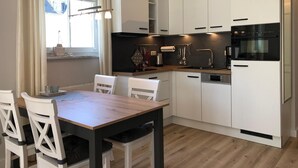 A modern kitchen with white cabinets, a wooden dining table, and a window with curtains. - (178) 3-room apartment Ostseeallee - apartment house Dünenschloss (Kühlungsborn)