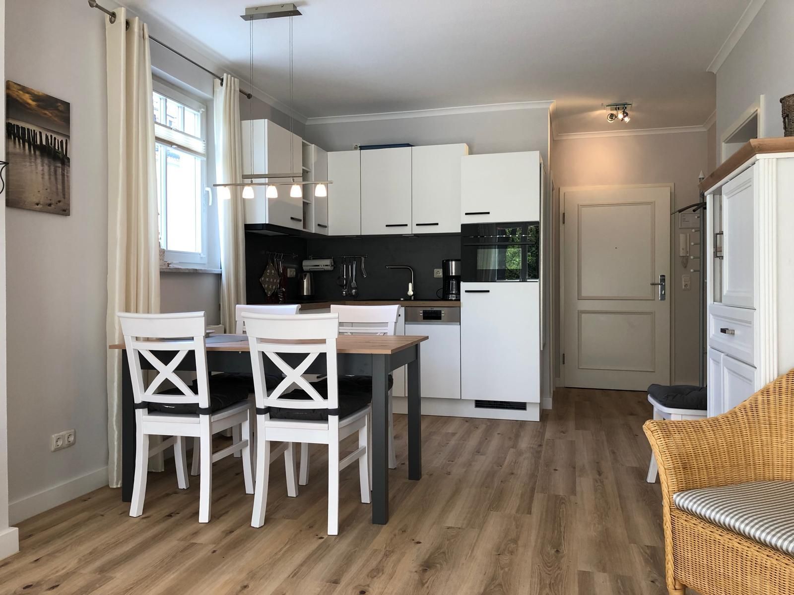 A modern kitchen with white cabinets, a dining table with four chairs, and a wicker chair in the corner.